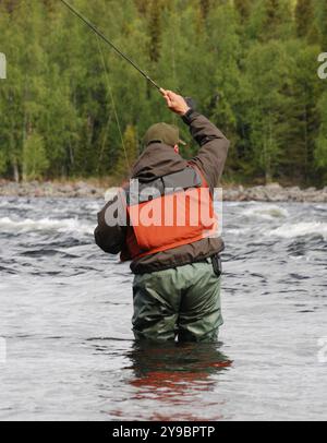 Fisherman trägt Wathose und eine orange Schwimmweste, während er in einem schnell fließenden Fluss steht Stockfoto