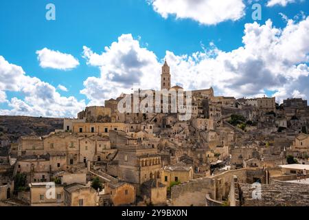 Eingebettet in die Hügel bietet Matera Italien atemberaubende Steinbauten und eine reiche Geschichte unter einem faszinierenden Himmel voller flauschiger Wolken, die Reisende einladen, seinen Charme und sein Erbe zu entdecken. Stockfoto