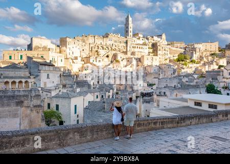 Ein Paar steht Hand in Hand und bestaunt die atemberaubende Landschaft von Matera in Apulien, Italien, wo antike Steinbauten majestätisch gegen einen dramatischen Himmel ragen. Stockfoto