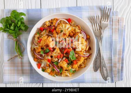 Gebratener Blumenkohl-Quinoa-Salat mit Walnüssen, roter Paprika, Zwiebeln und Koriander in weißer Schüssel auf weißem Holztisch mit Gabeln, flach liegend, schließen Stockfoto
