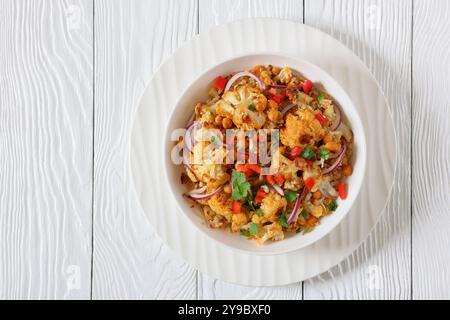 Gebratener Blumenkohl-Quinoa-Salat mit Walnüssen, rotem Pfeffer, Zwiebeln und Koriander in weißer Schüssel auf weißem Holztisch, horizontaler Blick von oben Stockfoto