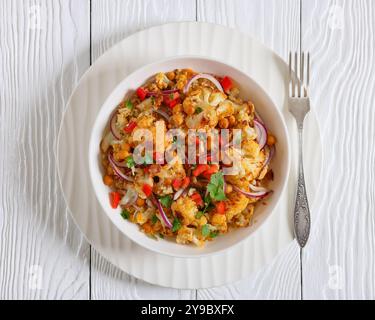 Gebratener Blumenkohl-Quinoa-Salat mit Walnüssen, rotem Pfeffer, Zwiebeln und Koriander in weißer Schüssel mit Gabel auf weißem Holztisch, horizontale Ansicht Stockfoto