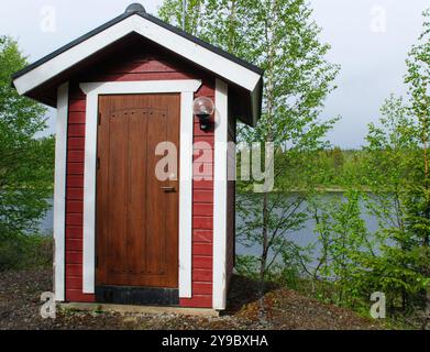 Kleines rotes Holzgebäude am Ufer eines Sees, umgeben von Birken, an einem Sommertag im skandinavischen Wald Stockfoto