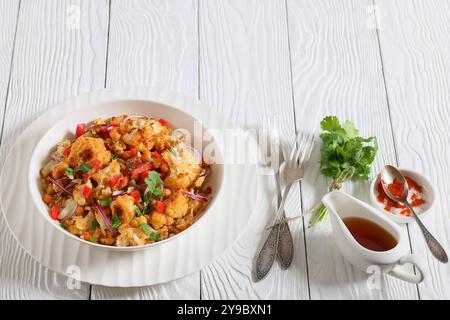 Gebratener Blumenkohl-Quinoa-Salat mit Walnüssen, rotem Pfeffer, Zwiebeln und Koriander in weißer Schüssel auf weißem Holztisch mit Gabeln, horizontale Ansicht Stockfoto
