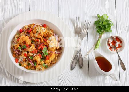 Gebratener Blumenkohl-Quinoa-Salat mit Walnüssen, rotem Pfeffer, Zwiebeln und Koriander in weißer Schüssel auf weißem Holztisch mit Gabeln, horizontale Ansicht Stockfoto