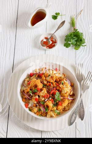 Gebratener Blumenkohl-Quinoa-Salat mit Walnüssen, rotem Pfeffer, Zwiebeln und Koriander in weißer Schüssel auf weißem Holztisch mit Gabeln, vertikale Ansicht f Stockfoto