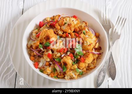 Gebratener Blumenkohl-Quinoa-Salat mit Walnüssen, rotem Pfeffer, Zwiebeln und Koriander in weißer Schüssel auf weißem Holztisch mit Gabeln, Nahaufnahme Stockfoto