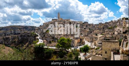Eingebettet in felsige Hügel, zeigt Matera seine atemberaubenden Höhlenwohnungen und historische Architektur, alle in wunderschönem Licht getaucht, während Wolken über den blauen Himmel gleiten und zu Entdeckungen und Staunen einladen. Stockfoto