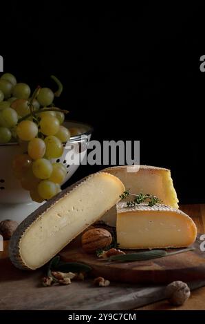 Bulgarischer Grünkäse auf schwarzem Hintergrund mit Trauben, Walnüssen und Kräutern Stockfoto