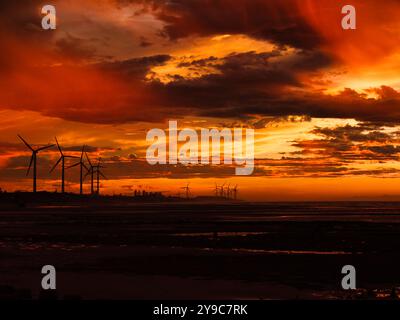 Feuriger Sonnenuntergang erfüllt den Himmel mit lebhaften Orange-, Rot- und Gelbtönen. Windräder stehen vor dem Horizont und schaffen eine Atmosphäre Stockfoto