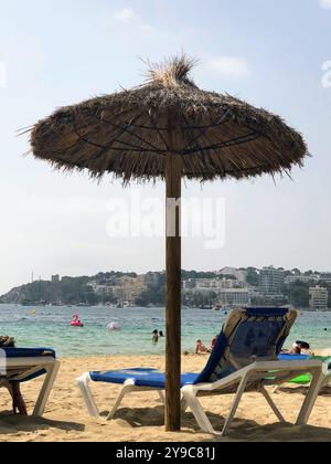 Eine ruhige Strandszene mit Strohschirm und Liegestühlen mit Blick auf das warme Wasser des Strands Palma Nova auf Mallorca Stockfoto