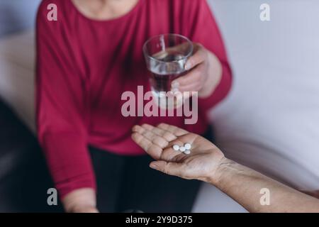 Eine ältere Frau sitzt auf ihrem Bett und ein Freiwilliger gibt ihr Pillen und ein Glas Wasser. Hochwertige Fotos Stockfoto