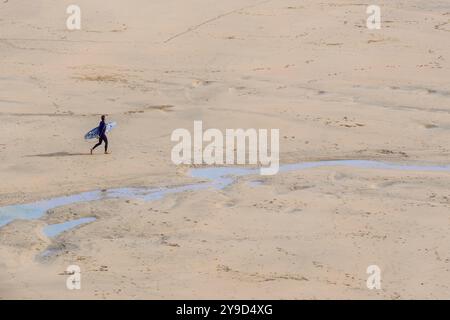 Ein einsamer Surfer mit seinem Surfbrett geht am Crantock Beach bei Ebbe an der Küste von Newquay in Cornwall in Großbritannien, Europa. Stockfoto