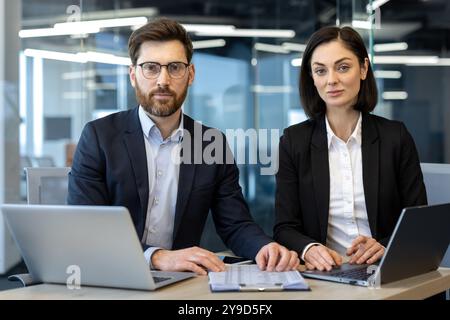Geschäftsleute, die im Büro sitzen und ein Notebook mit Sicherheit aussehen. Teamwork-Konzept mit moderner Technologie, Zusammenarbeit und Produktivität in der Unternehmensumgebung. Stockfoto
