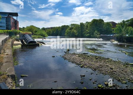 Das Foto zeigt den Fluss Ayr, der durch die Stadt Ayr fließt. Schöner klarer, sonniger Tag. Blick nach Osten flussaufwärts, vorbei am Ayrshire College Wehr und Fischleiter. Ta Stockfoto