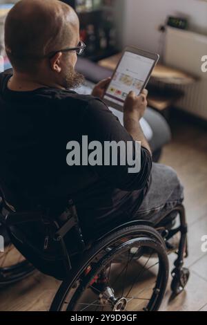 Ein junger Mann sitzt auf einem Stuhl mit einem Tablet, das online spricht. Hochwertige Fotos Stockfoto