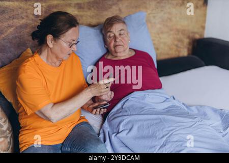 Eine Krankenschwester überprüft den Blutzuckerspiegel eines älteren Mannes, während sie neben ihm sitzt und mit einer Nadel in den Finger stochst. Hochwertige Fotos Stockfoto