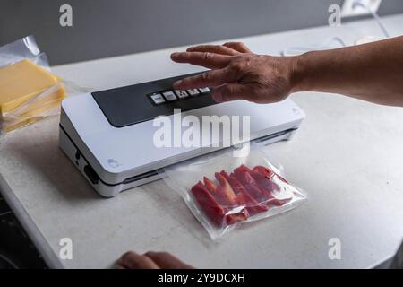 Vakuumverpackung der Versiegelungsmaschine mit Plastikbeutel mit rotem Pfeffer am weißen Tisch, Großaufnahme. Hochwertige Fotos Stockfoto