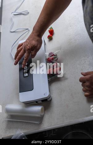 Die Hand eines Mannes benutzt eine Vakuummaschine, um Erdbeeren in Plastiktüten zu saugen. . Hochwertige Fotos Stockfoto