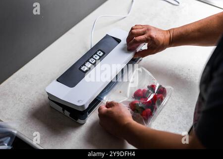 Die Hand eines Mannes benutzt eine Vakuummaschine, um Erdbeeren in Plastiktüten zu saugen. . Hochwertige Fotos Stockfoto