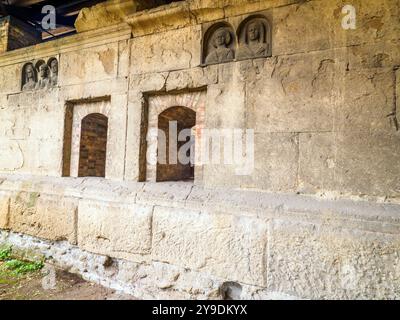 Das Detail des Grabes „Gemino Sepulchre“, das auf sechs verschiedene Freigelassene der Familien Clodia, Marcia und Annia Bezug nimmt und auf den Anfang des 1. Jahrhunderts v. Chr. datiert ist, besteht aus zwei Zellen, die über kleine Türen zugänglich sind, die sich nach außen auf eine Fassade öffnen, die von einem Tufffuß mit Skulpturen von Verstorbenen gekennzeichnet ist. Republikanische Gräber an der Via Statilia – Rom, Italien Stockfoto