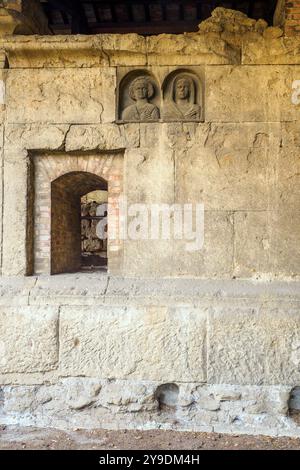 Das Detail des Grabes „Gemino Sepulchre“, das auf sechs verschiedene Freigelassene der Familien Clodia, Marcia und Annia Bezug nimmt und auf den Anfang des 1. Jahrhunderts v. Chr. datiert ist, besteht aus zwei Zellen, die über kleine Türen zugänglich sind, die sich nach außen auf eine Fassade öffnen, die von einem Tufffuß mit Skulpturen von Verstorbenen gekennzeichnet ist. Republikanische Gräber an der Via Statilia – Rom, Italien Stockfoto