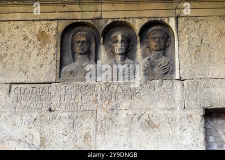 Das Detail des Grabes „Gemino Sepulchre“, das auf sechs verschiedene Freigelassene der Familien Clodia, Marcia und Annia Bezug nimmt und auf den Anfang des 1. Jahrhunderts v. Chr. datiert ist, besteht aus zwei Zellen, die über kleine Türen zugänglich sind, die sich nach außen auf eine Fassade öffnen, die von einem Tufffuß mit Skulpturen von Verstorbenen gekennzeichnet ist. Republikanische Gräber an der Via Statilia – Rom, Italien Stockfoto