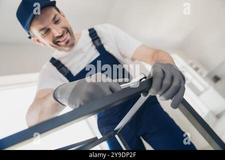 Ein lächelnder Handwerker in blauen Overalls führt Hausrenovierungen mit Werkzeugen durch, die professionelle Reparatur- und Wartungsfähigkeiten für das Haus vermitteln Stockfoto