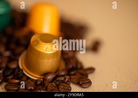 Detaillierte Ansicht mehrfarbiger Kaffeekapseln auf gerösteten Kaffeebohnen. Der Kontrast unterstreicht die Mischung aus Tradition und Komfort Stockfoto