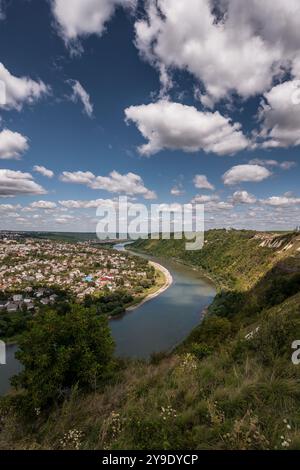 Ruhige Aussicht auf einen sich windenden Fluss, umgeben von üppigen grünen Hügeln und einer malerischen Stadt unter einem bewölkten Himmel. Stockfoto