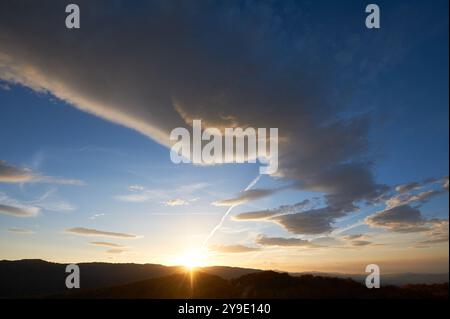 Der atemberaubende Sonnenuntergang erfüllt den Himmel mit satten Blau- und Orangetönen. Dramatische Wolken mit Anklängen von Rosa und Gold verteilen sich über den Himmel. Silhouetten von Hügeln im Vordergrund verleihen der atemberaubenden Abendszene Tiefe. Stockfoto