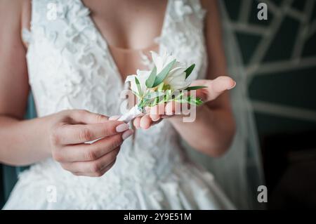Der zärtliche Moment einer Braut: Eine wunderschöne Blumenboutonnière halten. Stockfoto