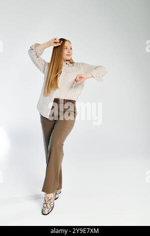 Eine selbstbewusste Frau zeigt ihren Sinn für Mode mit langen Haaren in einem gestreiften Outfit vor grauem Hintergrund. Stockfoto