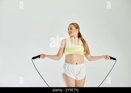 Eine fröhliche Frau trägt ein Crop Top und Shorts, während sie ein Seil überspringt und Energie im Studio ausstrahlt. Stockfoto