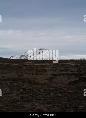 Verschneite Berge mit einer gewundenen Straße im Vordergrund, vor einem bewölkten Himmel und einer kargen, zerklüfteten Landschaft Stockfoto