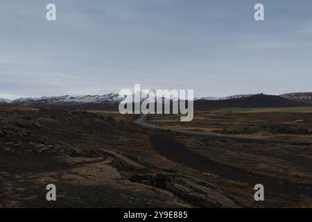 Verschneite Berge mit einer gewundenen Straße im Vordergrund, vor einem bewölkten Himmel und einer kargen, zerklüfteten Landschaft. Stockfoto