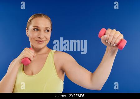 Eine fitte Frau hebt begeistert kleine Kurzhanteln und zeigt ihre Stärke in einer lebendigen Studioatmosphäre. Stockfoto