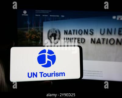 Person mit Smartphone und Logo der Organisation der Vereinten Nationen UN Tourismus auf dem Bildschirm vor der Website. Schwerpunkt auf dem Display des Telefons. Stockfoto