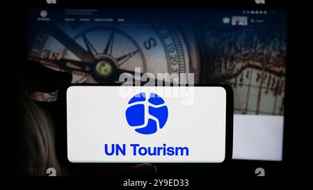 Person, die ein Handy hält, mit dem Logo der Organisation der Vereinten Nationen UNO Tourismus auf dem Bildschirm vor der Webseite. Schwerpunkt auf dem Display des Telefons. Stockfoto