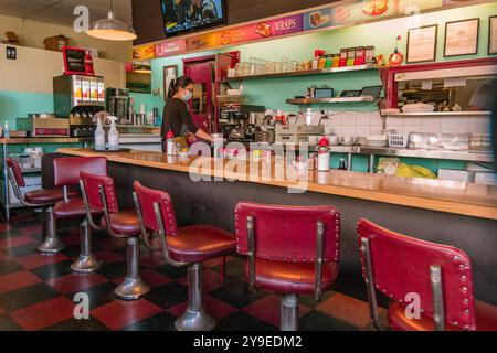 Vancouver, BC, Kanada-15. September 2023: Frau arbeitet hinter der Theke eines klassischen amerikanischen Restaurants mit roten Stühlen an der Theke. Stockfoto