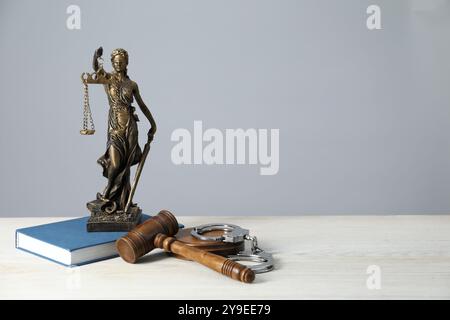 Handschellen, richterlicher Hammer, Lady Justice Figur und Buch auf weißem Holztisch, Platz für Text Stockfoto