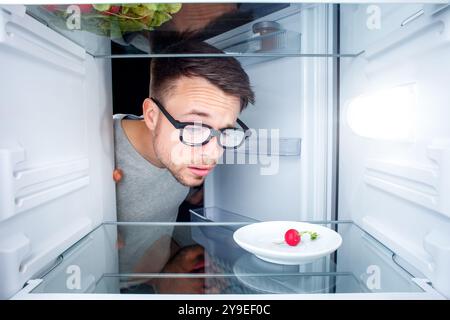 Ein verwirrter Mann, der in einen fast leeren Kühlschrank schaut Stockfoto