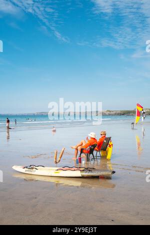 Zwei RNLI-Rettungsschwimmer sitzen in Stühlen und beobachten Urlauber im Meer bei Ebbe am GT Great Western Beach in Newquay in Cornwall in Großbritannien Stockfoto