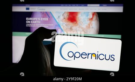 Person, die ein Smartphone mit dem Logo des ESA-Erdbeobachtungsprojekts Copernicus auf dem Bildschirm vor der Website hält. Schwerpunkt auf dem Display des Telefons. Stockfoto