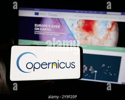 Person, die ein Mobiltelefon mit dem Logo des ESA-Erdbeobachtungsprojekts Copernicus auf dem Bildschirm vor der Webseite hält. Schwerpunkt auf dem Display des Telefons. Stockfoto