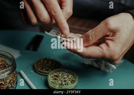 Nahaufnahme eines Mannes, der Tabak in ein Papierrollenpapier legt, wie er einen Joint macht, bevor er den Tabak mit etwas zerfetztem Cannabis mischt Stockfoto