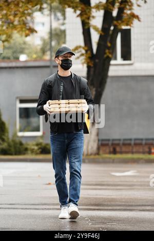 Ein Liefermann betritt ein Bürogebäude und trägt mehrere Essensbestellungen, während er eine schwarze Maske trägt. Stockfoto