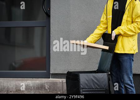 Ein Liefermann mit schwarzer Maske kommt in einem Bürogebäude an und trägt eine Bestellung für den viel befahrenen Arbeitsplatz. Stockfoto