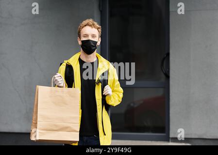 Ein Liefermann in schwarzer Maske bringt tagsüber eine große Bestellung in ein geschäftiges Bürogebäude. Stockfoto