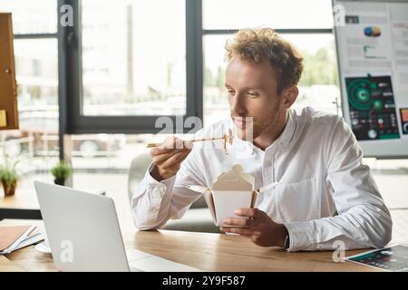 Der rothaarige Geschäftsmann, gekleidet in einem knusprigen weißen Hemd, arbeitet nachdenklich an seinem Projekt während des Mittagessens. Stockfoto